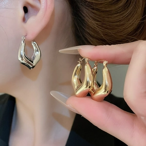 Detailed view of chunky geometric U-shaped metal earrings in polished gold and silver