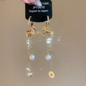 Détail macro de boucles d'oreilles cheval à bascule doré avec perles et poinçon argent