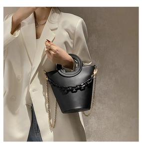 Chic black bucket bag with resin chain detail and gold chain strap held by a model