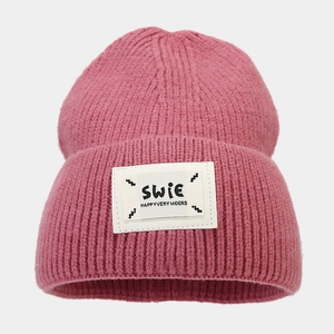 Close-up of rose pink ribbed knit beanie with decorative white square patch detail