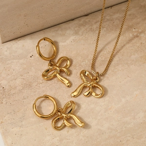 Elegant gold bow necklace and earrings set displayed on a natural beige stone surface