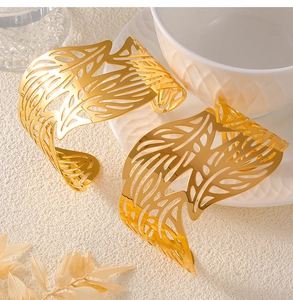 Detail of gold-plated leaf hollow cuff bracelet resting on a minimalist white ceramic bowl