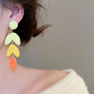 Detail of three-tier raffia tassel earrings with green, yellow, and orange gradient tones