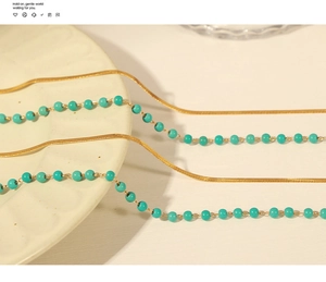 Detailed view of layered gold snake chain and turquoise bead necklace on a white plate