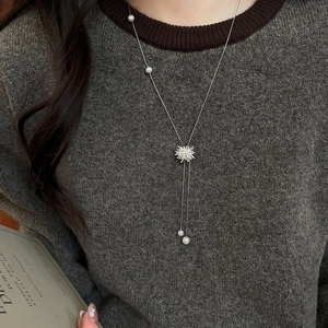 Détail d'un collier de perles argenté avec pendentif flocon sur un pull gris chic