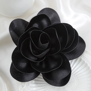Detail of handmade 3D black fabric rose brooch with textured matte petals on silk
