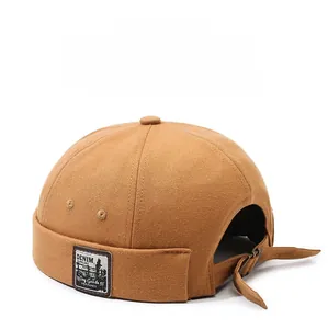 Detail of brown cotton brimless dock cap showing denim text label and metal strap buckle