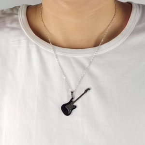 Close-up of a black guitar pendant necklace on a model wearing a white t-shirt