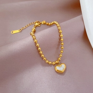 Macro detail of gold beaded bracelet with heart-shaped mother of pearl charm on silk