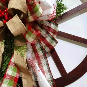 Close-up of rustic Christmas wreath with red plaid bow and pine cone on wooden wheel