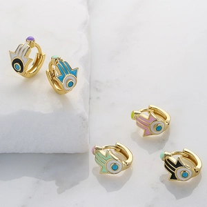 Golden Hamsa Hand hoop earrings with colorful enamel devil eye charms on marble surface