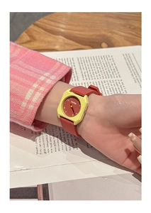 Detail showing a stylish red silicone watch on a wrist against a book background