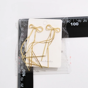 Detailed size measurement of golden bow tassel earrings with ruler on white card