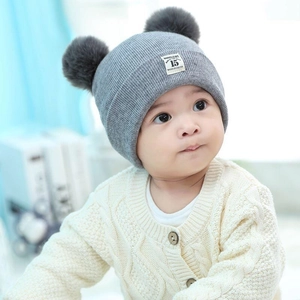Detailed close-up of grey baby knit hat with double faux fur pom-poms on an infant