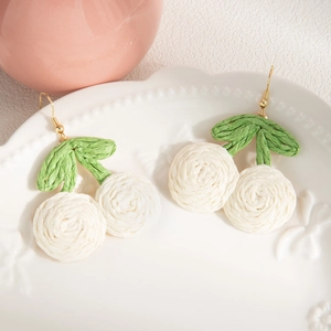 Macro shot of handmade woven white cherry earrings on an elegant white embossed plate