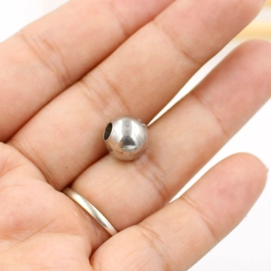 Polished stainless steel round spacer bead held in palm to show compact size for DIY