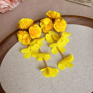 Detail view of yellow chiffon flower tassel earrings on a textured wooden jewelry tray