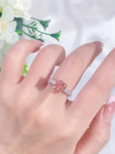 Detailed shot of a large square orange-pink gemstone ring set in a silver band on a finger