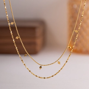 Detail of a layered gold tassel necklace featuring delicate diamond charms and metallic discs