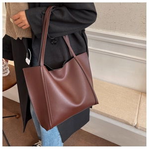 Detail of a large dark brown leather tote bag showing rich texture and side profile on model