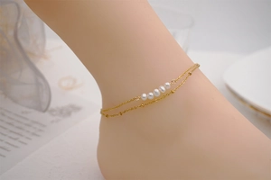 Detail of double-layer gold titanium anklet featuring five white freshwater pearls on a model