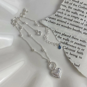 Minimalist silver chain necklace featuring heart and circle charms on a textured background