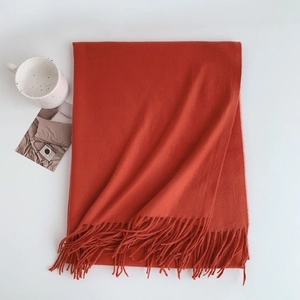 Detail of soft orange-red cashmere-like scarf with fringe edges next to a white mug