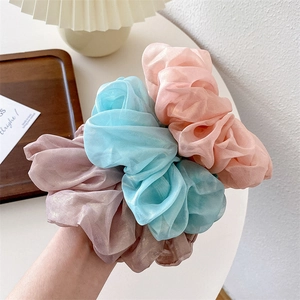 Detailed view of three iridescent organza scrunchies in pink, blue and purple
