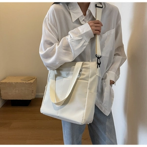 Detail of off-white canvas tote bag featuring adjustable strap and front zipper pocket