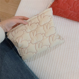 Detail of cute rabbit embroidery on a cream quilted makeup bag with a woven brand label