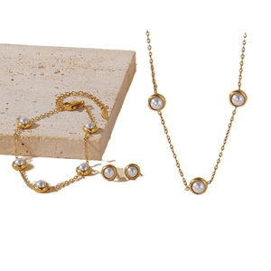 Elegant gold titanium steel jewelry set featuring round white pearls on stone background
