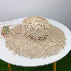 Flat lay of a wide brim straw sun hat with frayed edges on a white table for summer travel