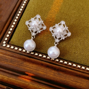 Macro detail of retro hollow silver earrings with pavé zircons and white drop pearls