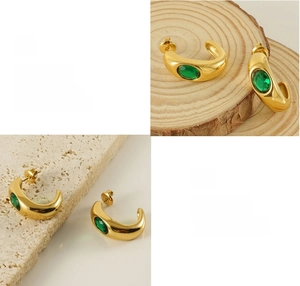 Detail of C-shaped gold-plated earrings featuring oval green zircon on stone background