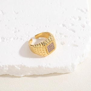 Macro shot of gold square purple zircon ring with braided texture on a stone plate