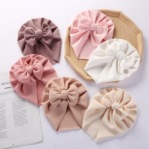 Detail of baby waffle knit bow hats in pink, white, and khaki on a wooden tray