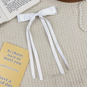 Close-up of white satin bow hair clip with long ribbons on a vintage plaid tablecloth