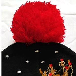 Close-up of a black knit Christmas hat featuring a fluffy red pompom and crown pattern