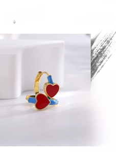 Macro shot of gold heart earrings with vibrant red enamel and blue drip oil details