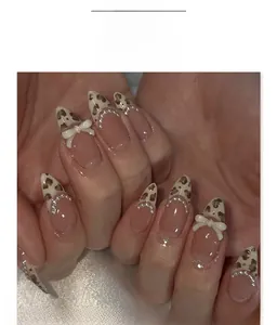 Détail de faux ongles amande avec motif léopard, nœuds blancs et petites perles
