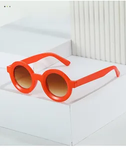 Close-up of bright orange round sunglasses with gradient brown lenses on white blocks