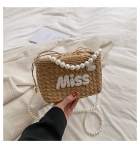 Detail of beige woven beach bag with pearl handle and MISS letter decoration