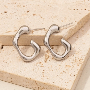 Macro shot of silver 304 stainless steel C-shaped earrings on a textured beige stone plate