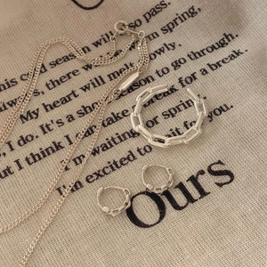 Close-up of knotted hollow 925 silver ring and matching jewelry set on linen fabric