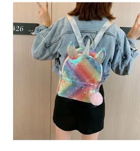 Girl wearing a sequin unicorn backpack with rainbow colors and a pink fur pompom
