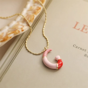 Détail macro du collier à chaîne dorée avec pendentif lettre G en émail rose et rouge