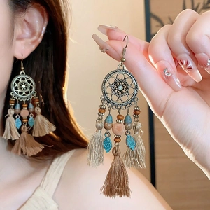 Détail de boucles d'oreilles bohèmes vintage avec disque floral en bronze et glands beige