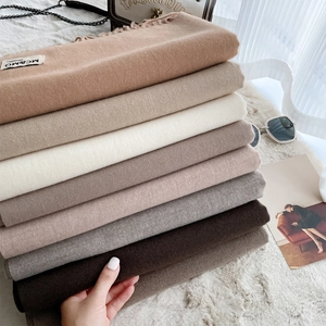 Soft solid cashmere feel fringe scarves in assorted earth tones stacked on a plush rug