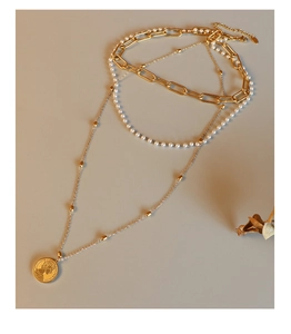 Macro detail of triple-layered titanium necklace with pearls and engraved coin pendant