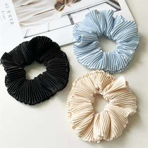Close-up of pleated satin scrunchies in black, light blue, and beige on a fashion magazine